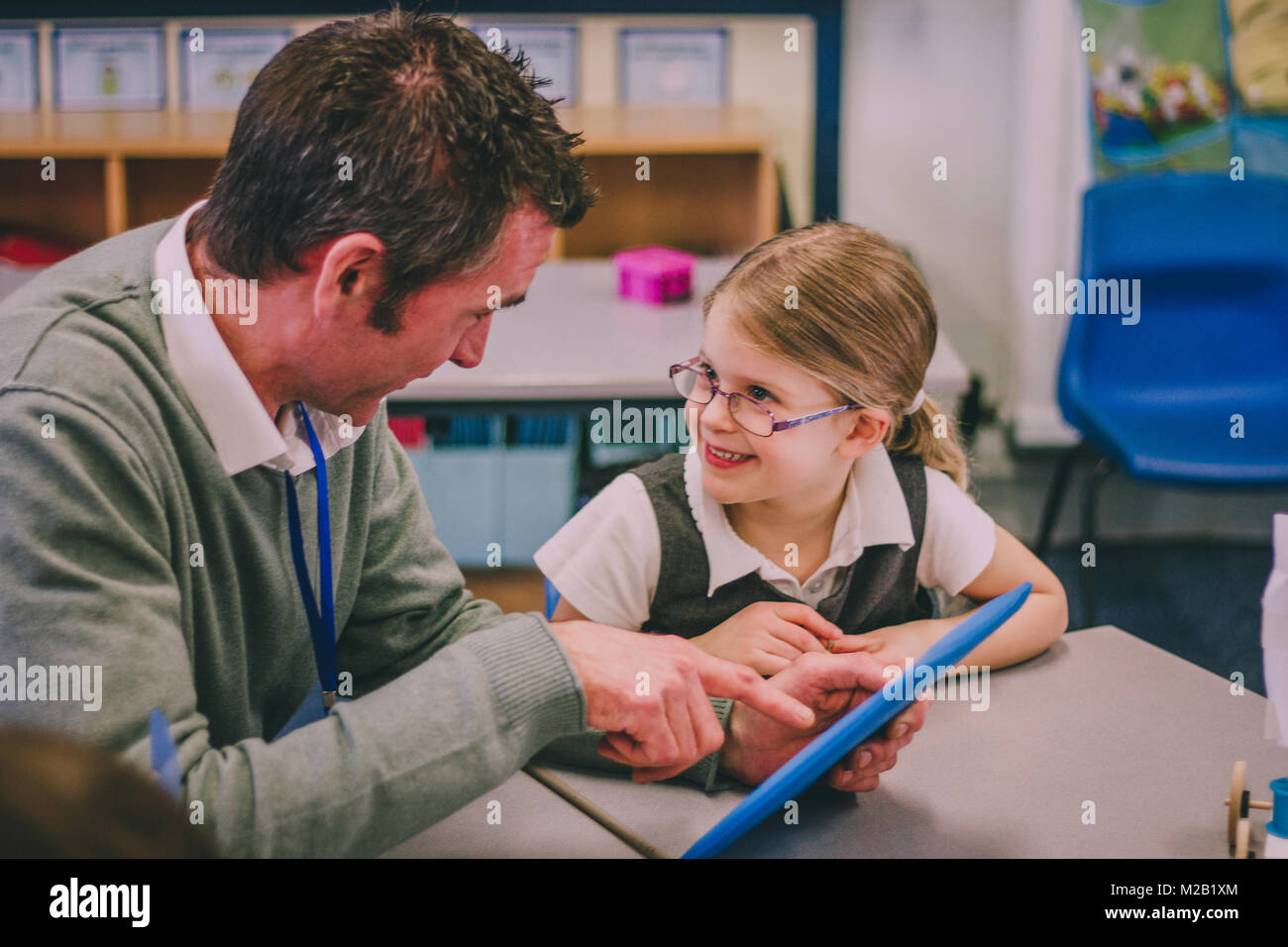 Male teacher is using a digital tablet with his student in a classroom ...