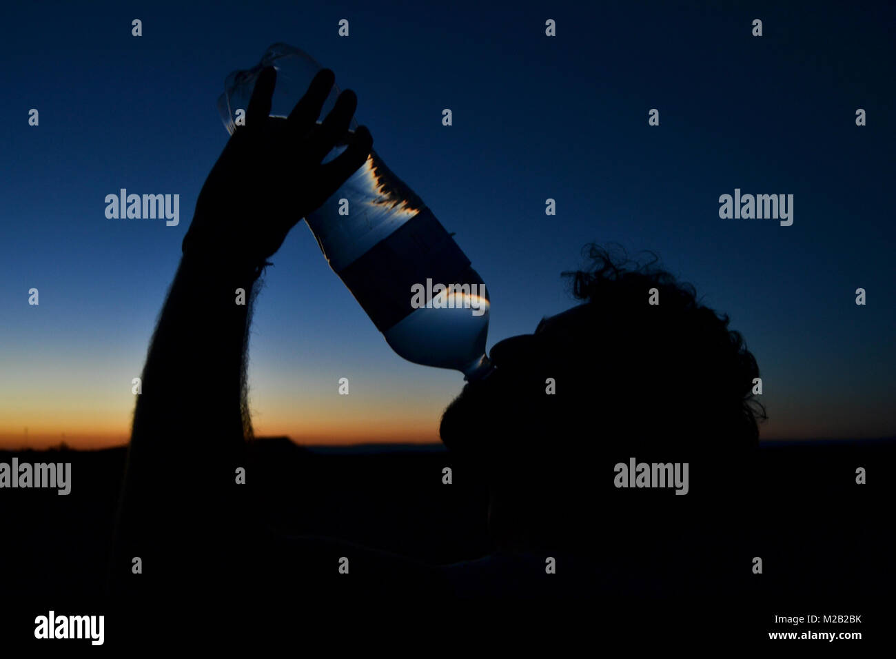 Young man drinking bottled water during sunset in the desert Stock