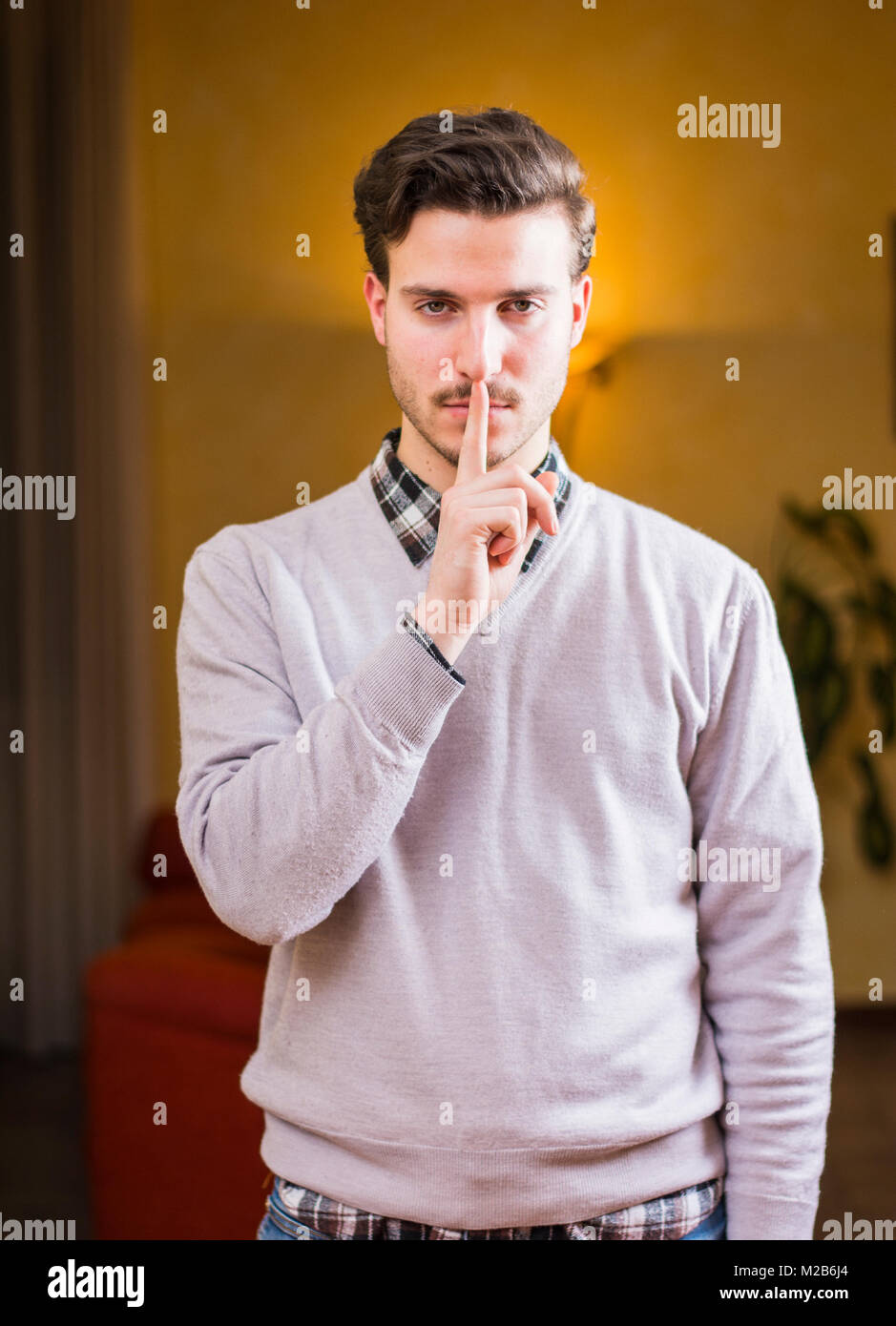 Handsome young man doing Hush sign with finger on lips Stock Photo - Alamy
