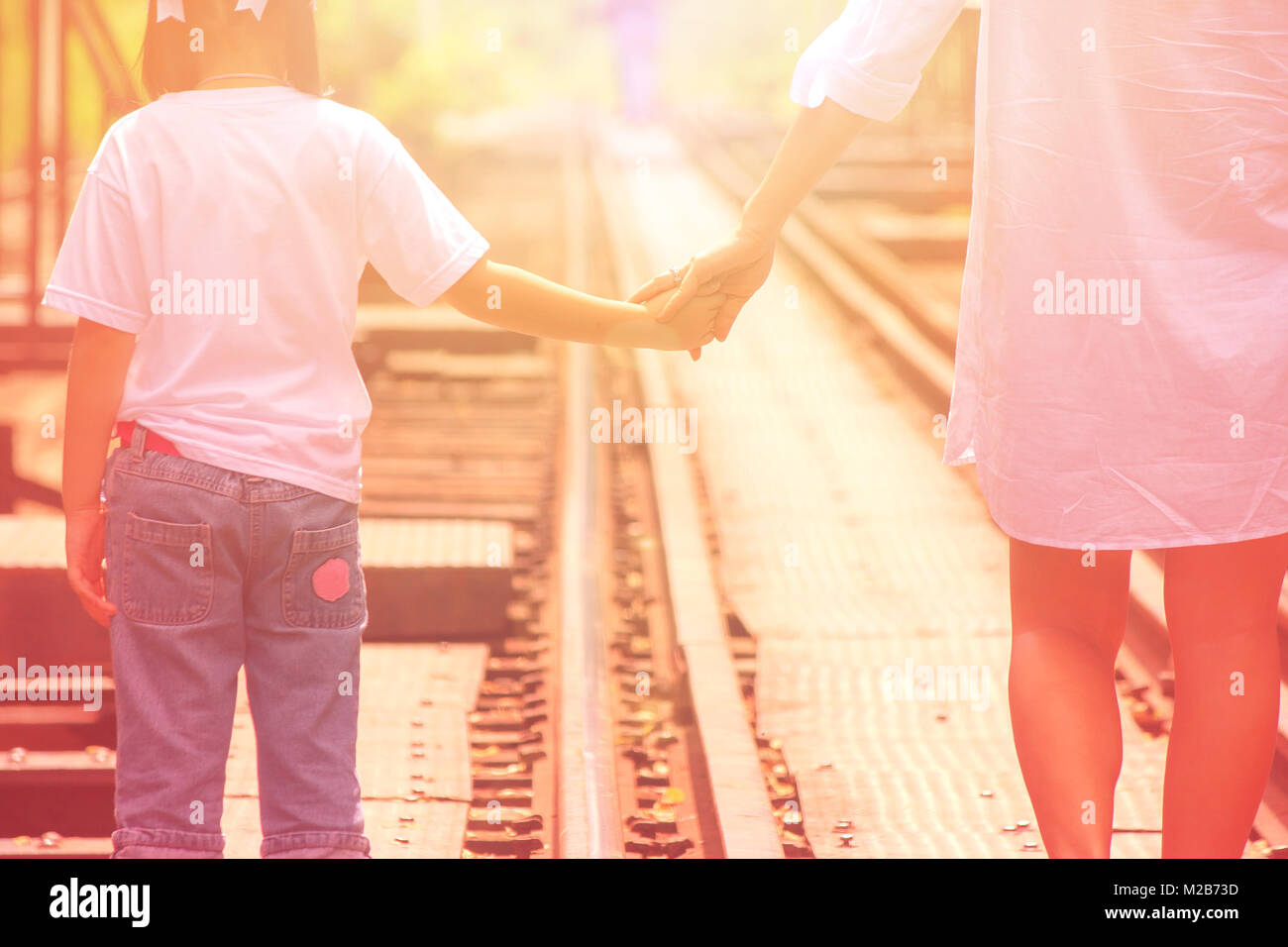 Adorable Family Concept : Woman and children walking on railroad tracks and holding hand together with sun flare background. Stock Photo
