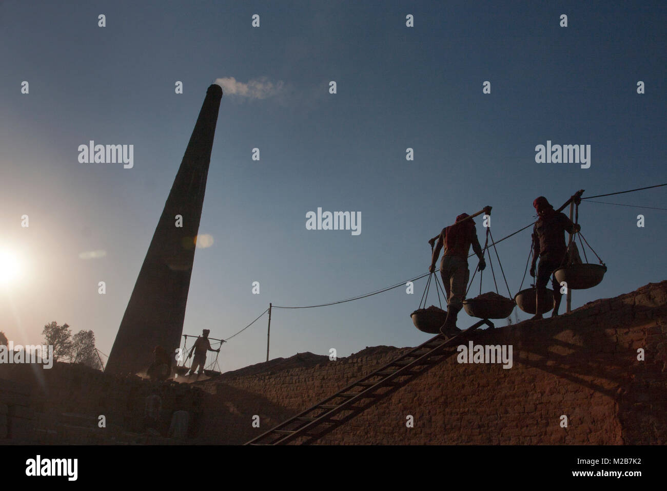 Men carry dust from the base of the kiln to the surface in a brick factory in Nepal. Stock Photo