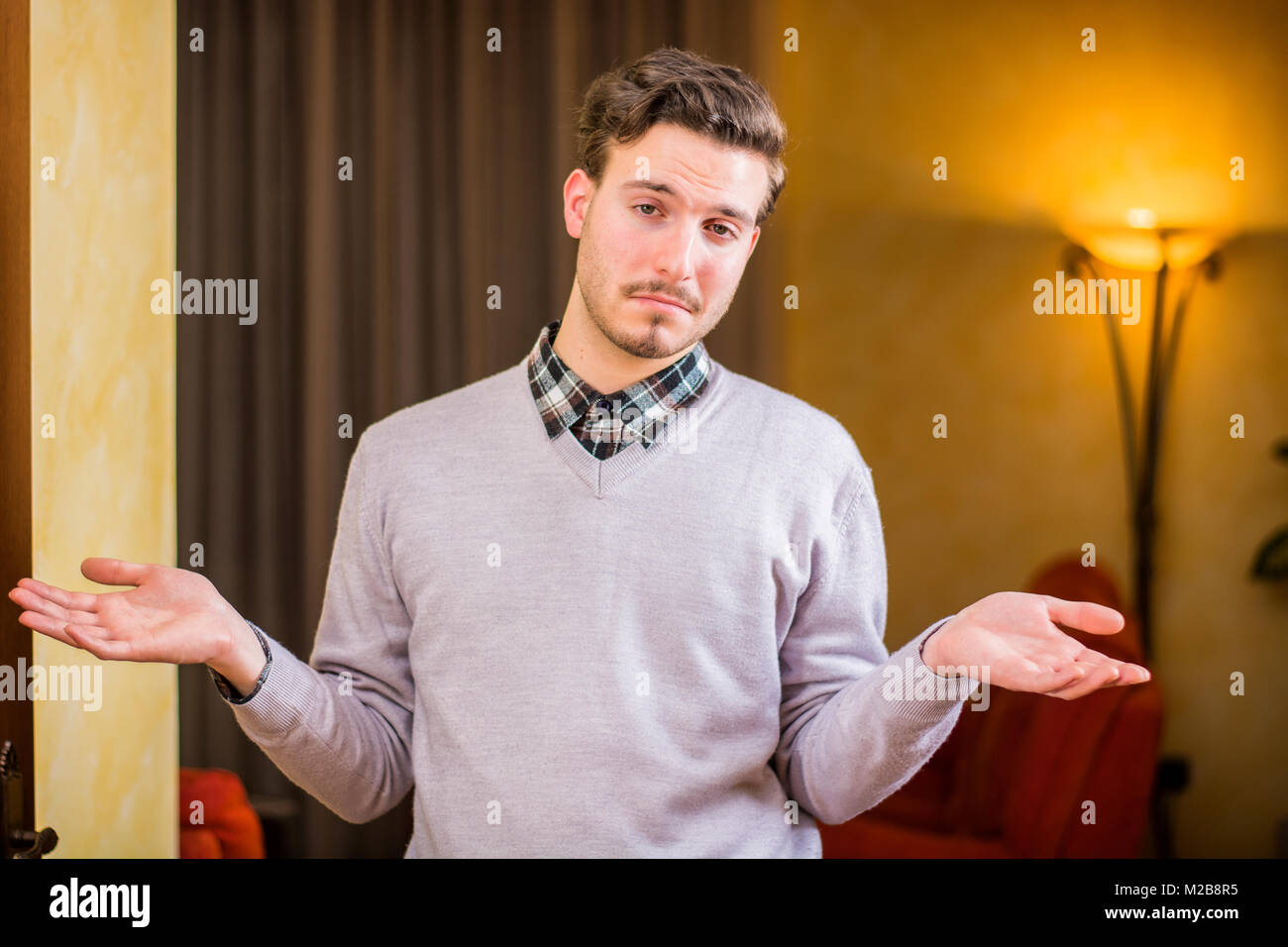 Confused or doubtful young man shrugging with palms open Stock Photo