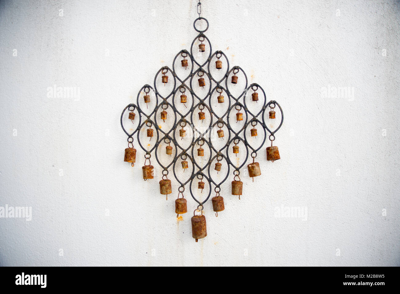 Ornamental metal wind chime with small rusty bells hanging on a white wall Stock Photo