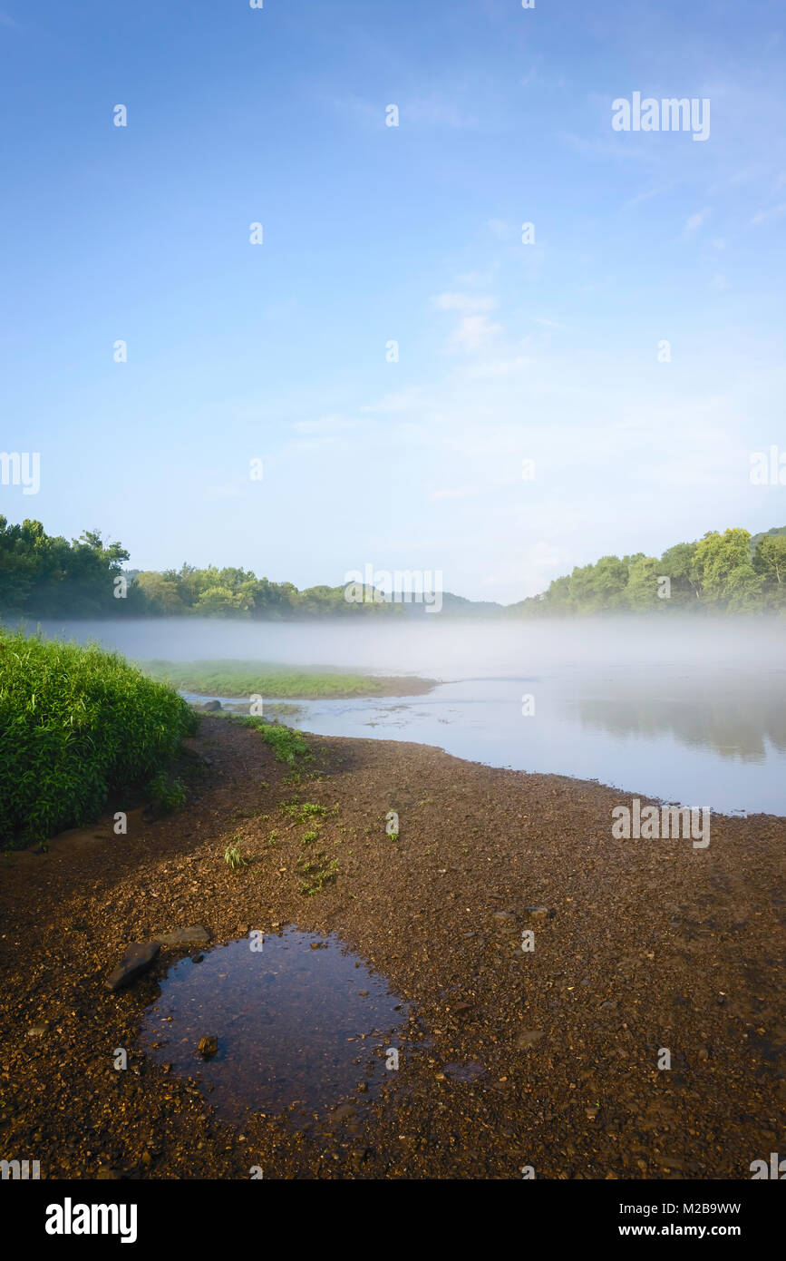 Morning mist lifts over the Little Tennessee river flanked by trees and stony bank near Gatlinburg, Tennessee, USA. Stock Photo