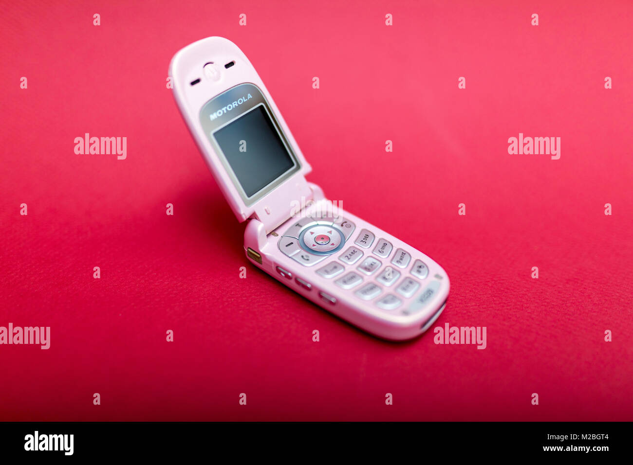 Cool and classic Motorola V220 pink retro flip cell or mobile phone isolated against a red background Stock Photo