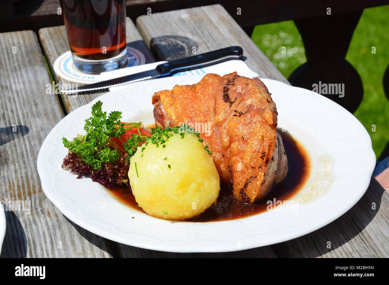 Schweinshaxe served with fried potatoes (Bratkartoffeln) and Sauerkraut at a Bavarian restaurant in the mountains above Tegernsee. Stock Photo