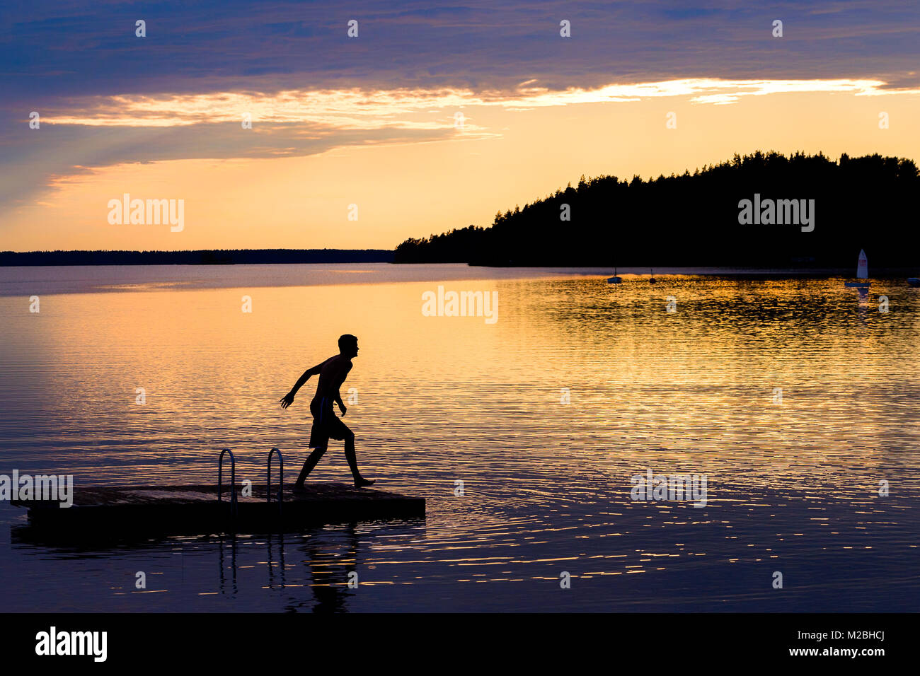 Silhouette of young man jumping from a pontoon into lake at sunset Stock Photo