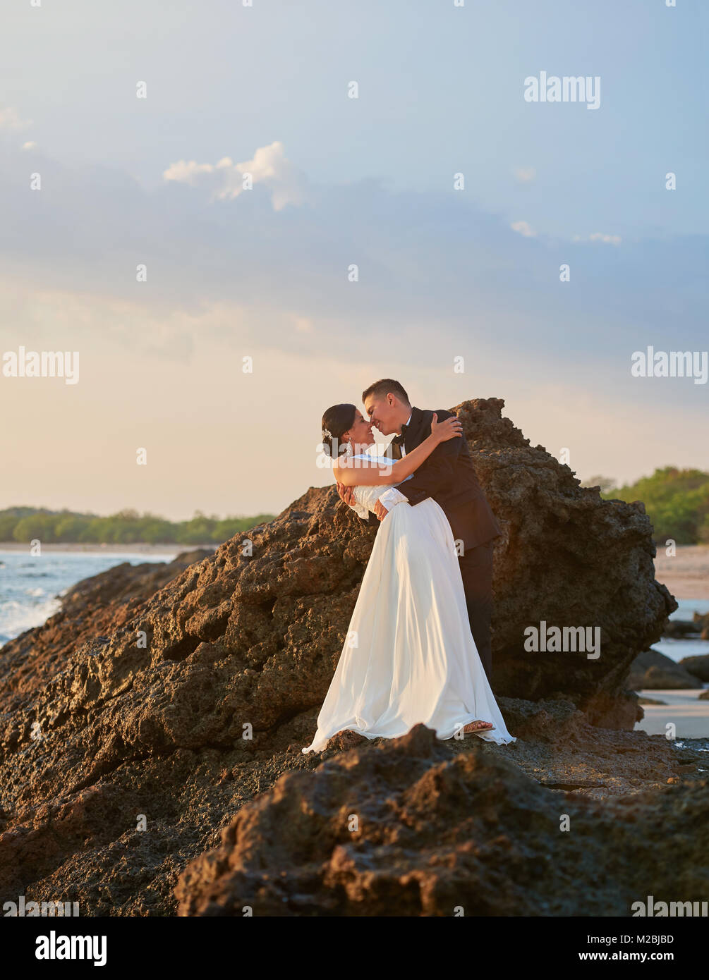 Young bride and groom kiss on sunset at ocean coast. Romantic marriage ...