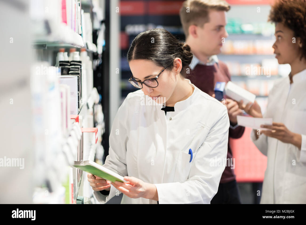 Portrait of a female experienced pharmacist reading the indications from the package of a new pharmaceutical product during work in a contemporary dru Stock Photo