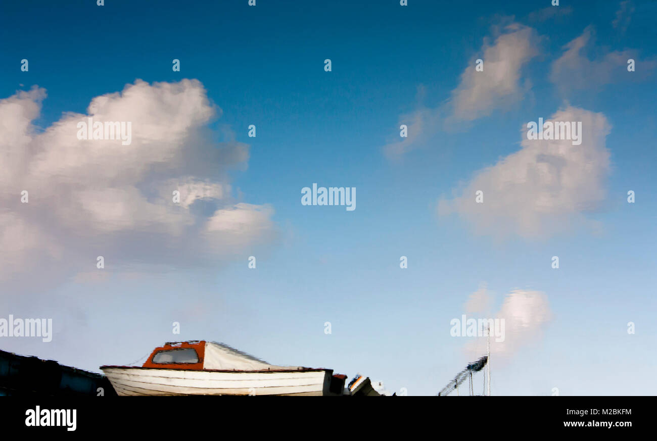 Blurry reflection of anchored small boats, blue sky and clouds in river water Stock Photo