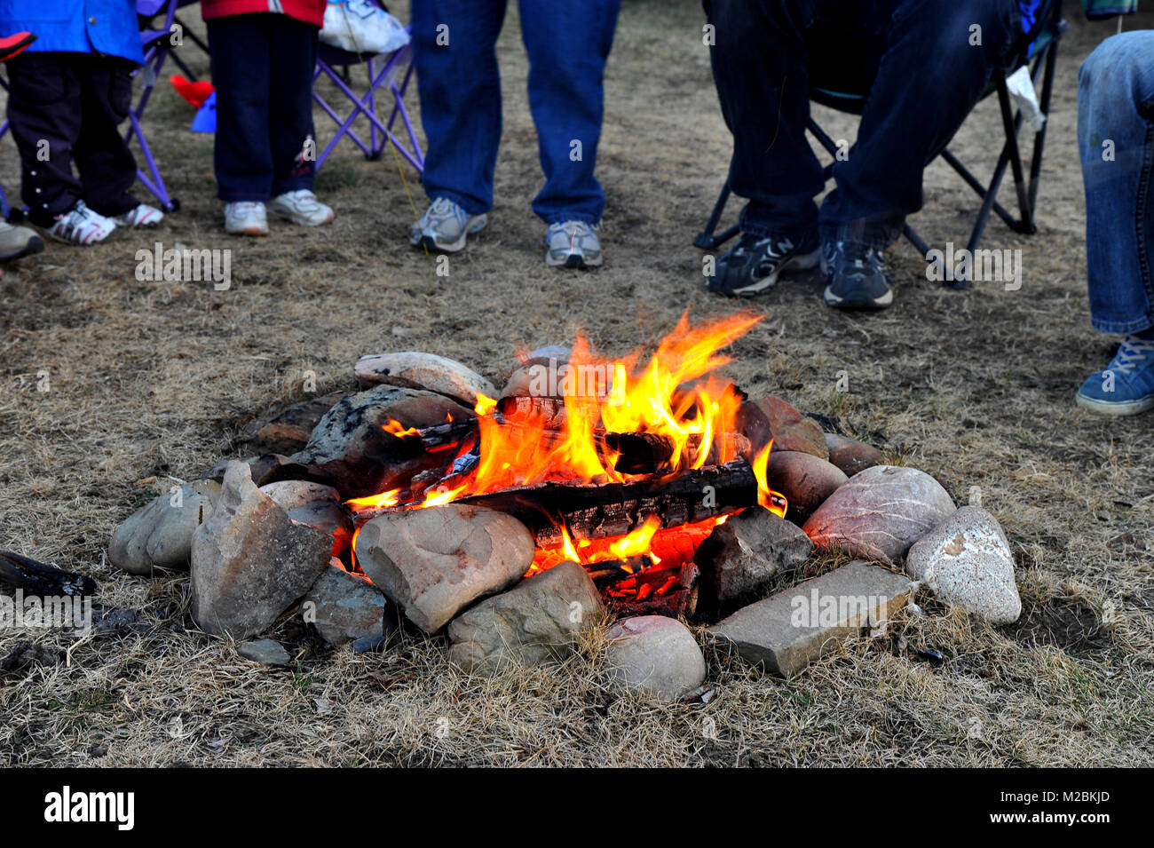 A camp fire in the safety of a stone circle with people gathered around in rural Alberta Canada. Stock Photo