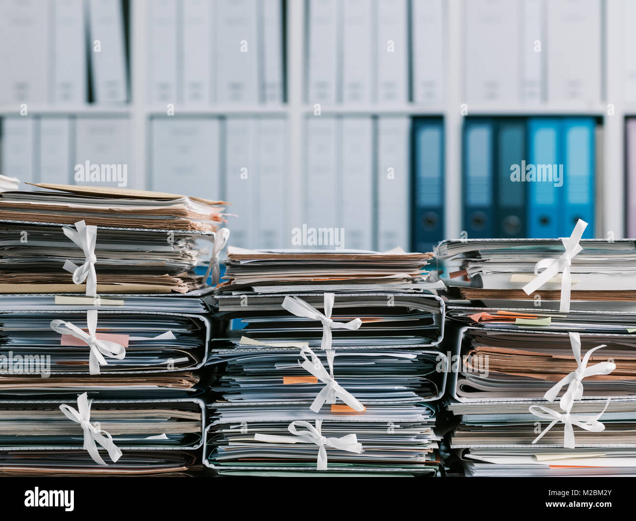 Stacks of files and paperwork in the office and bookshelves on the background: management and storage concept Stock Photo