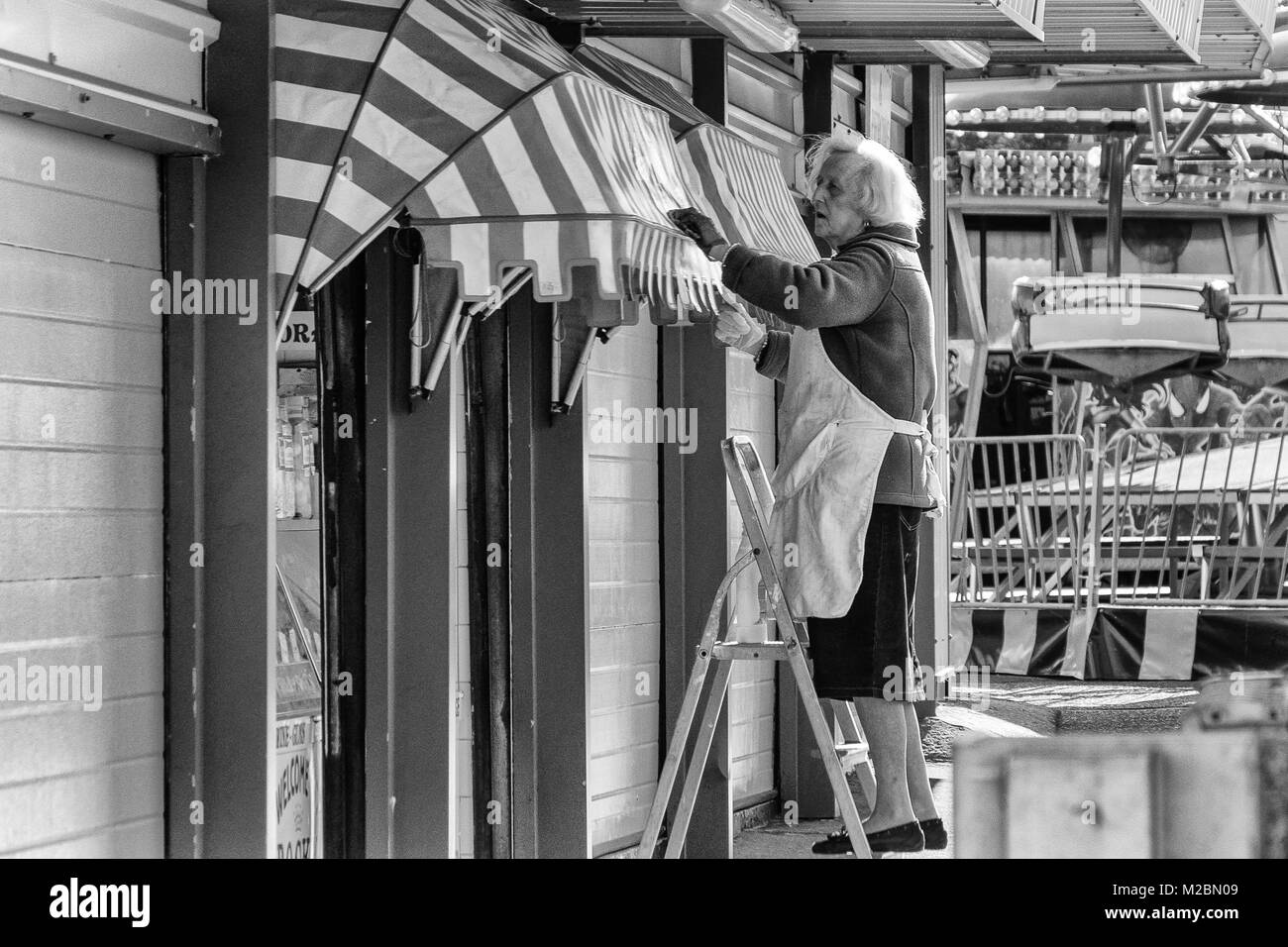 Old lady cleaning her chip shop front at Hunstanton Stock Photo