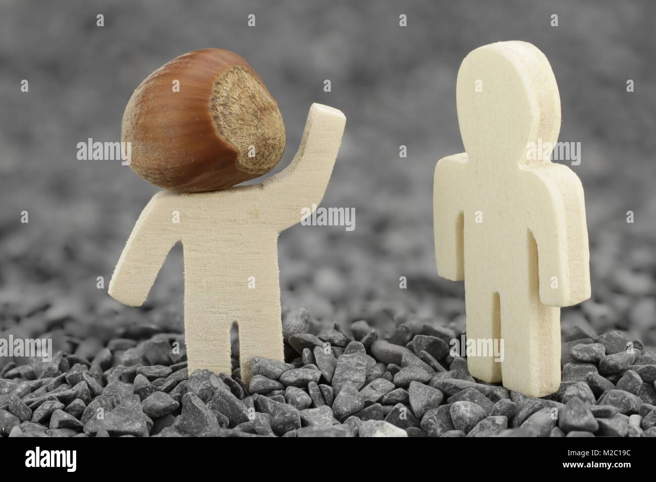 Wooden male with hazelnut as head waves to another Stock Photo