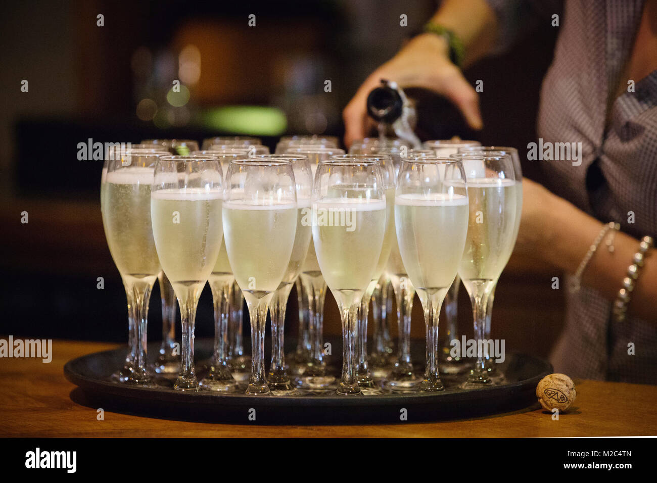 Person pouring champagne into champagne flutes, mid section, close-up Stock Photo