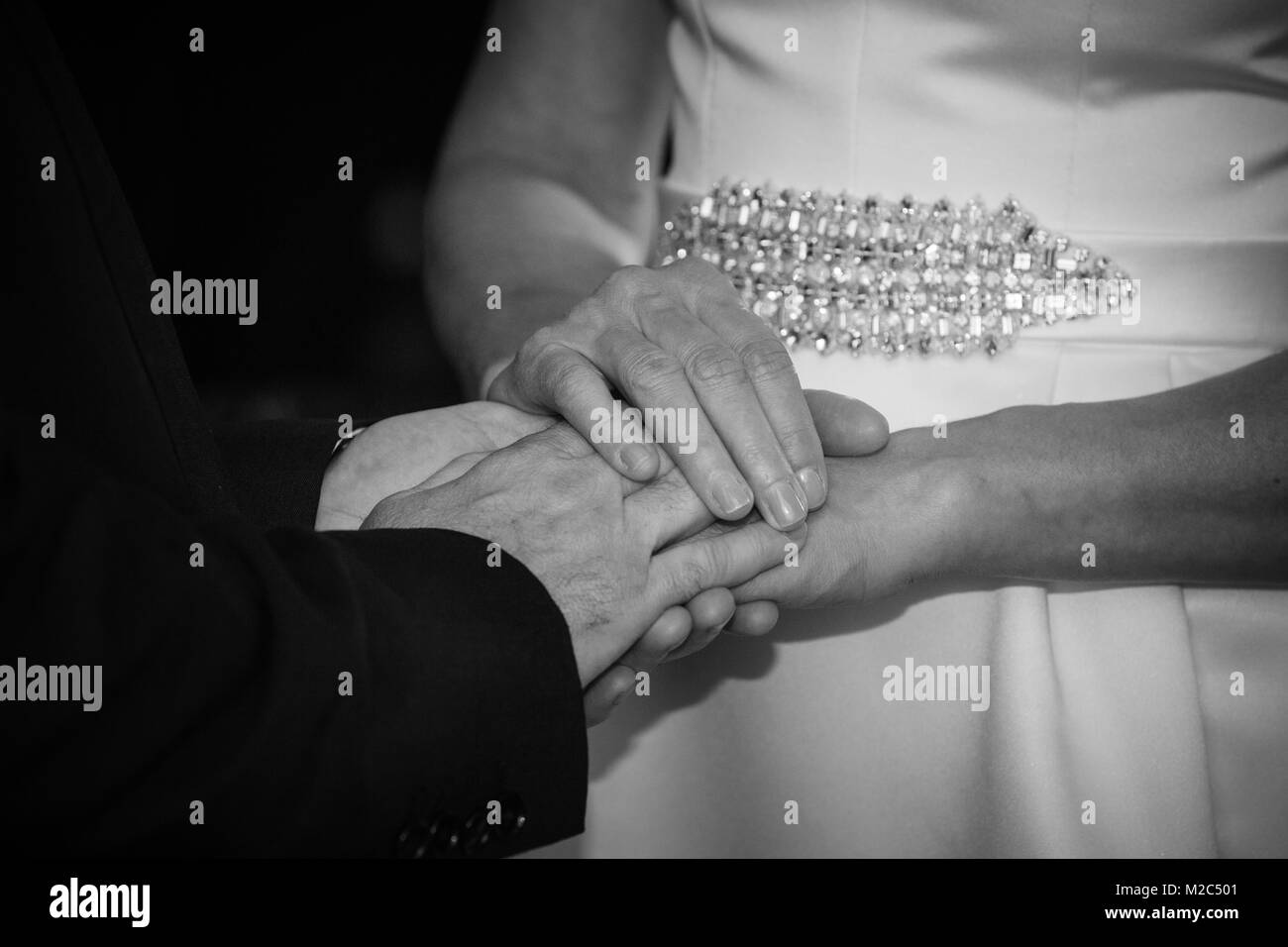 Bride and groom exchanging vows, holding hands, mid section, close-up, black and white Stock Photo