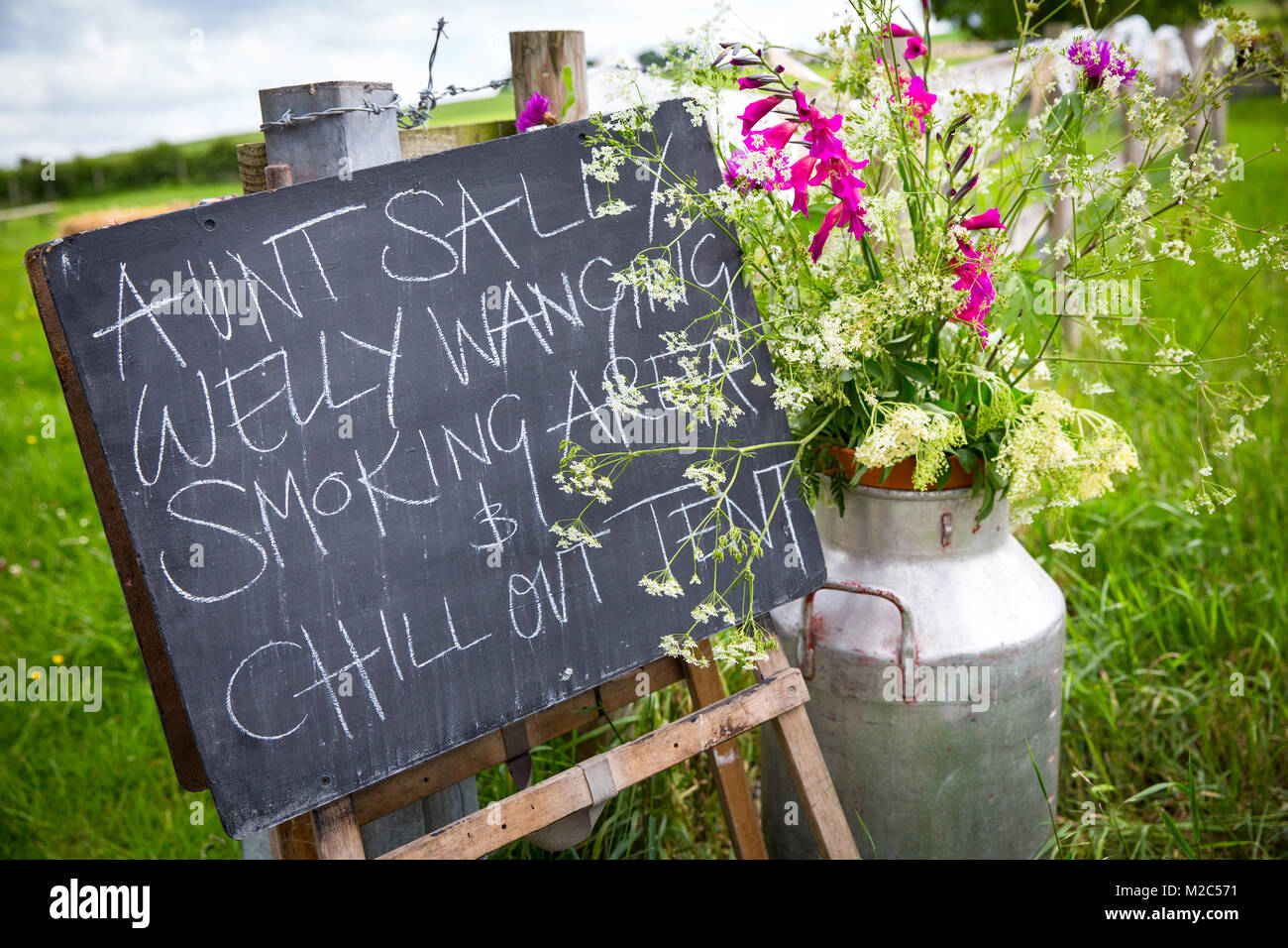 Chalkboard sign with milk churn filled with flowers, close-up Stock Photo