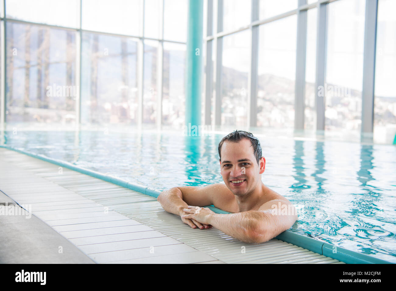 Man At Pool Young man relaxing on a luxury rooftop swimming pool and smiling at ...