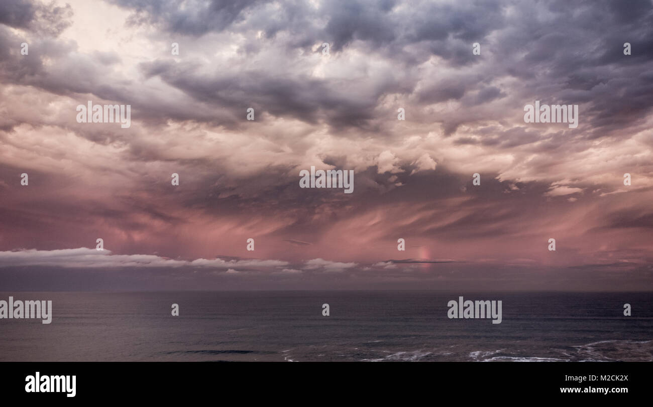 Stormy sky and vertical rainbow over the sea at sunset. Stock Photo