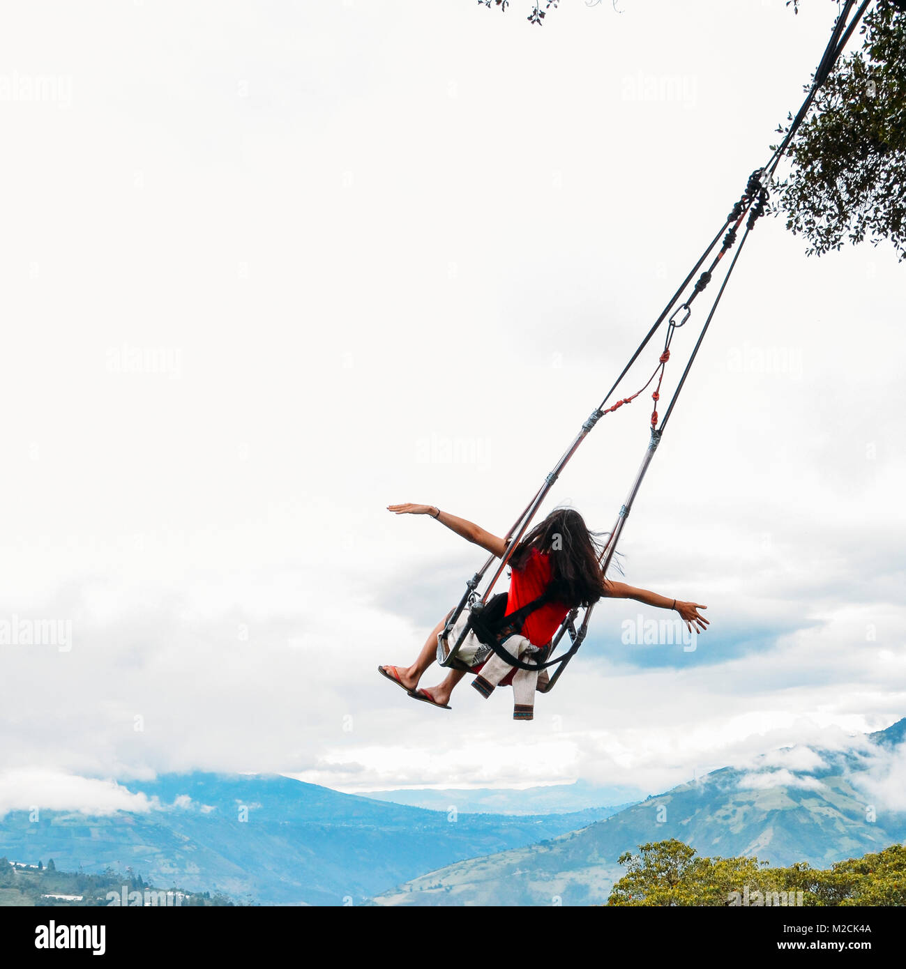 Young girl with arms outstretched rides a swing overlooking the landscape of Tungurahua, Ecuador Stock Photo