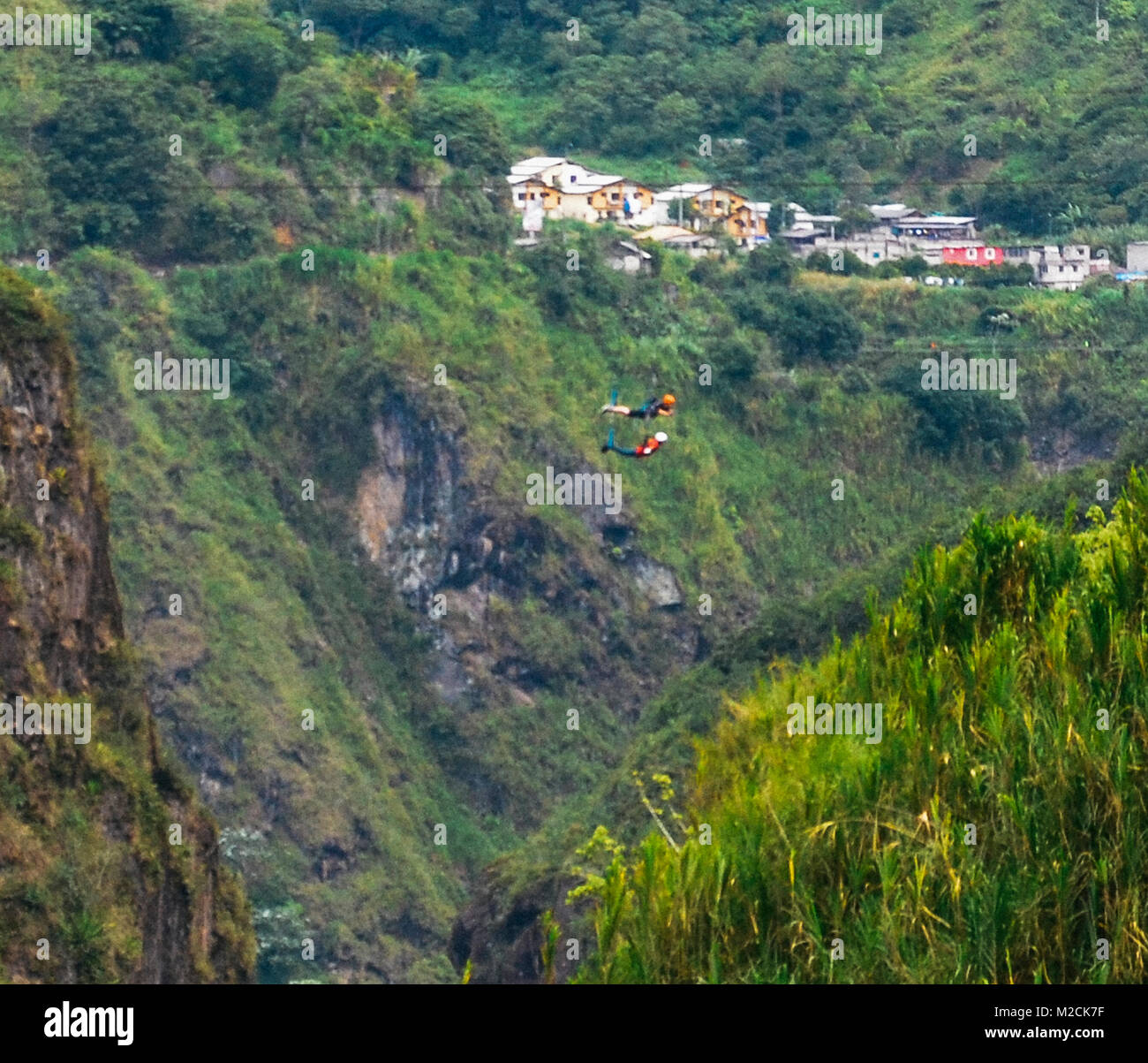 Two men cross a cascade on a zipline in Tungurahua, Ecuador, South America Stock Photo