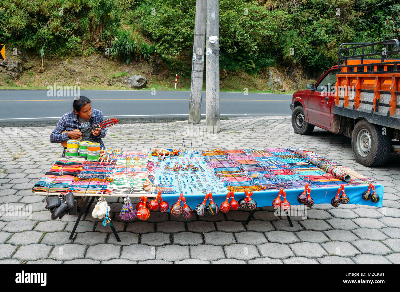 Local indigenous Ecuadorian man plays the banjo while selling local handicrafts on side of road Stock Photo