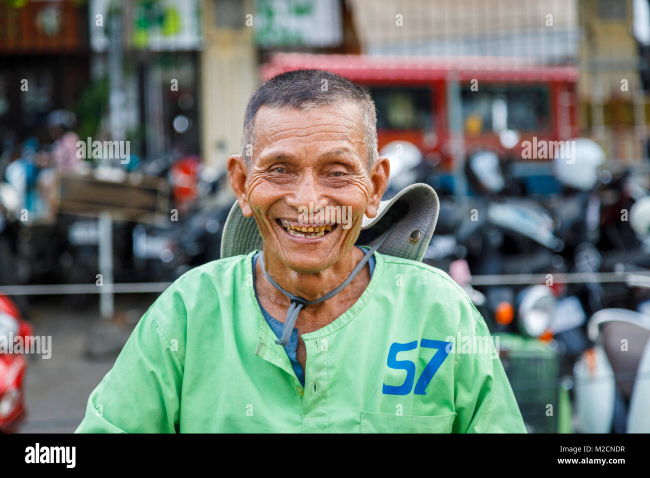 Happiness: joyful, friendly local Cambodian Cyclo City Tour cycle rickshaw driver with bad teeth in a green shirt in Phnom Penh, capital of Cambodia Stock Photo