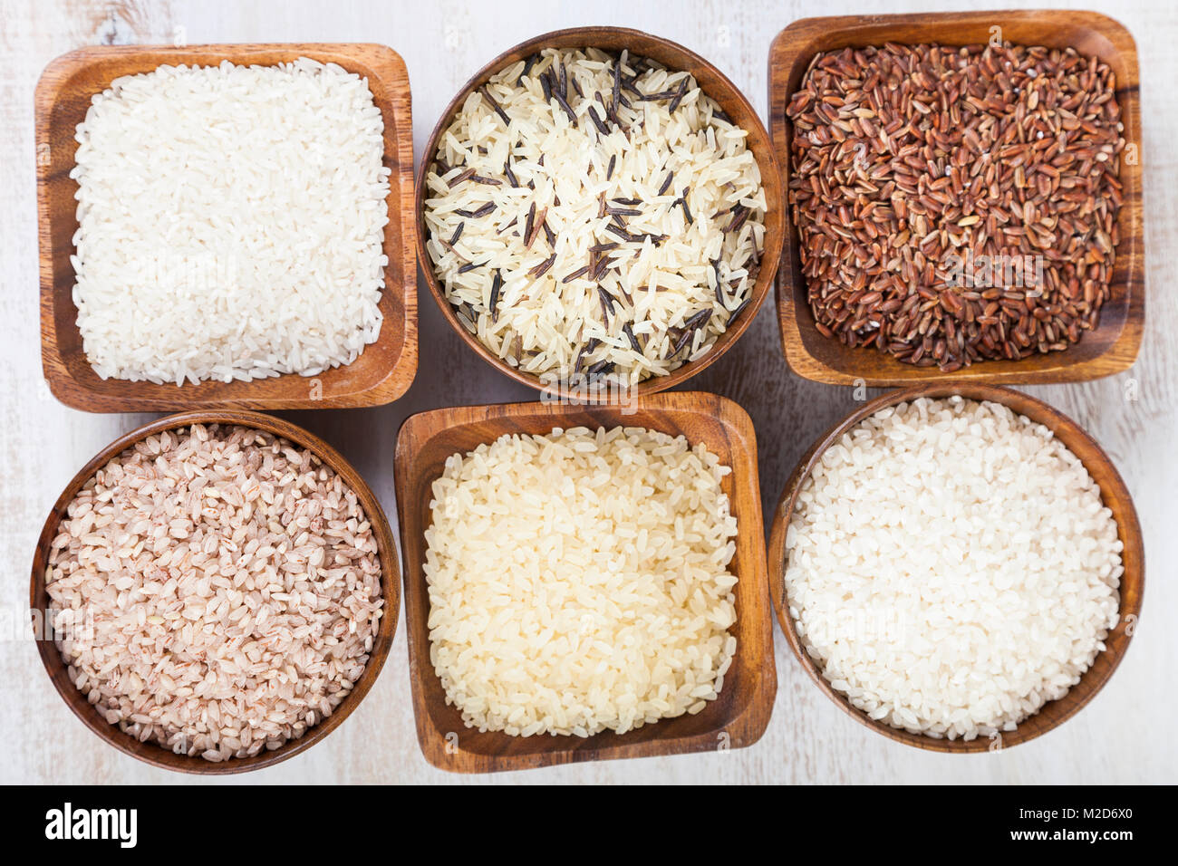 Six bowls with different varieties of rice on a wooden background ...