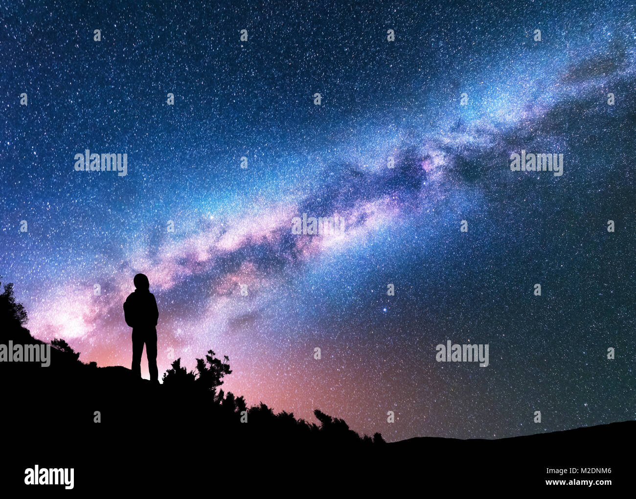 Silhouette of man with backpack on the hill against colorful Milky Way at night. Space background. Landscape with man, bright milky way, sky with star Stock Photo