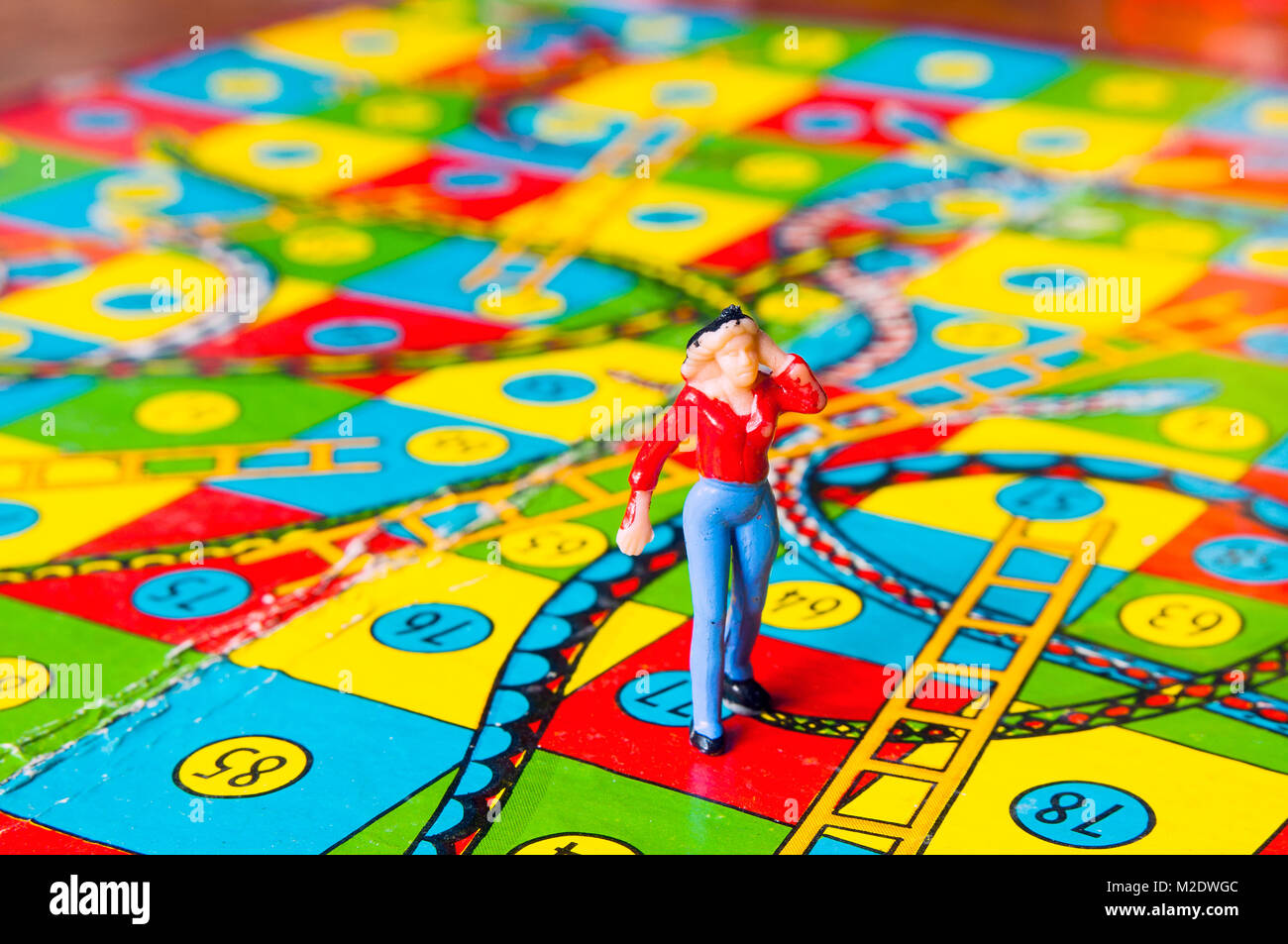 Retro Snakes and ladders board with miniature human figure in studio setting, Melbourne, Australia Stock Photo