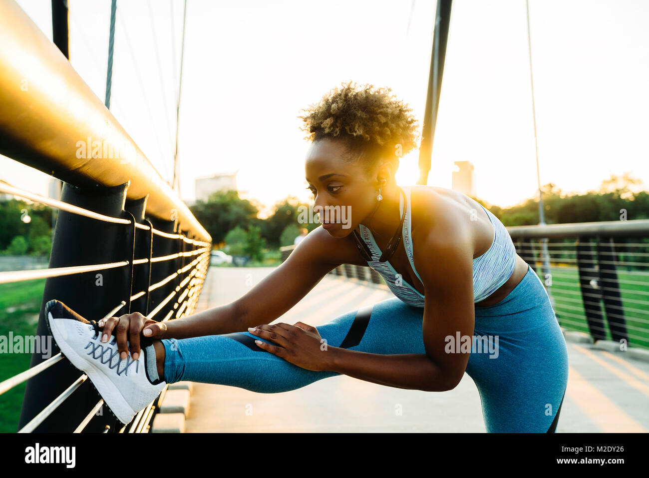 Mixed race woman stretching leg on bridge railing Stock Photo