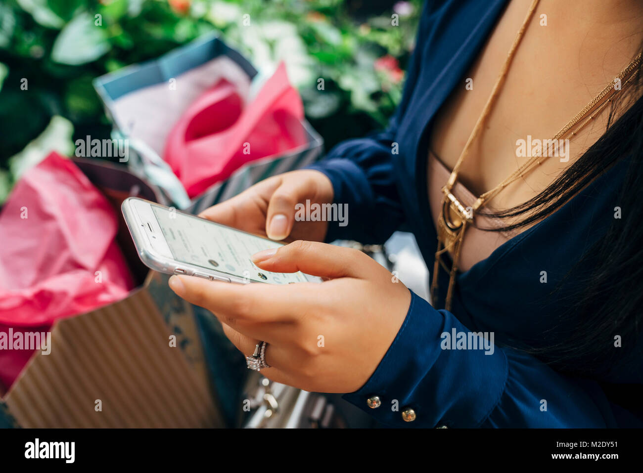 Hands of Hispanic woman with shopping bags texting on cell phone Stock Photo