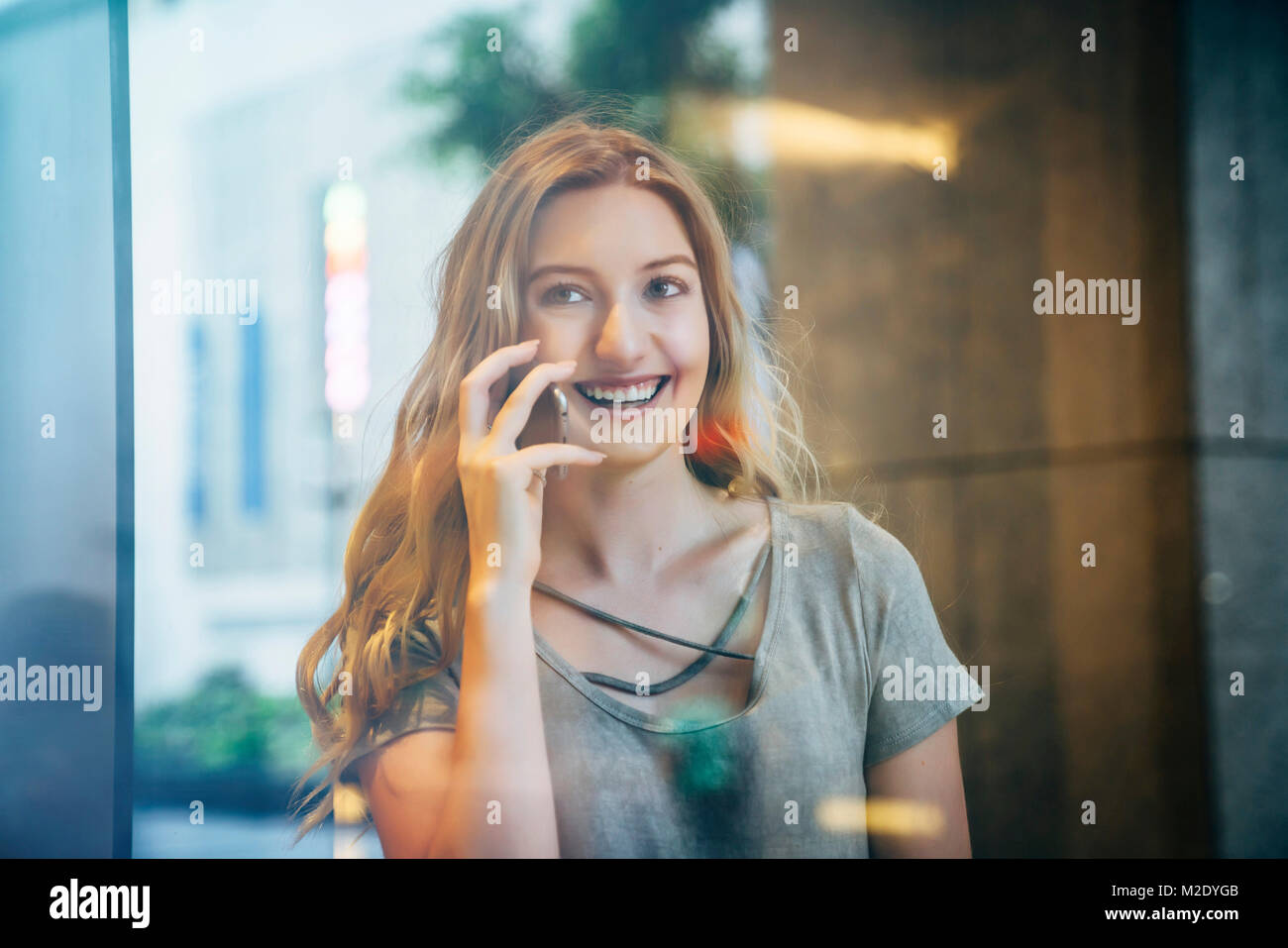 Smiling Caucasian woman talking on cell phone behind window Stock Photo
