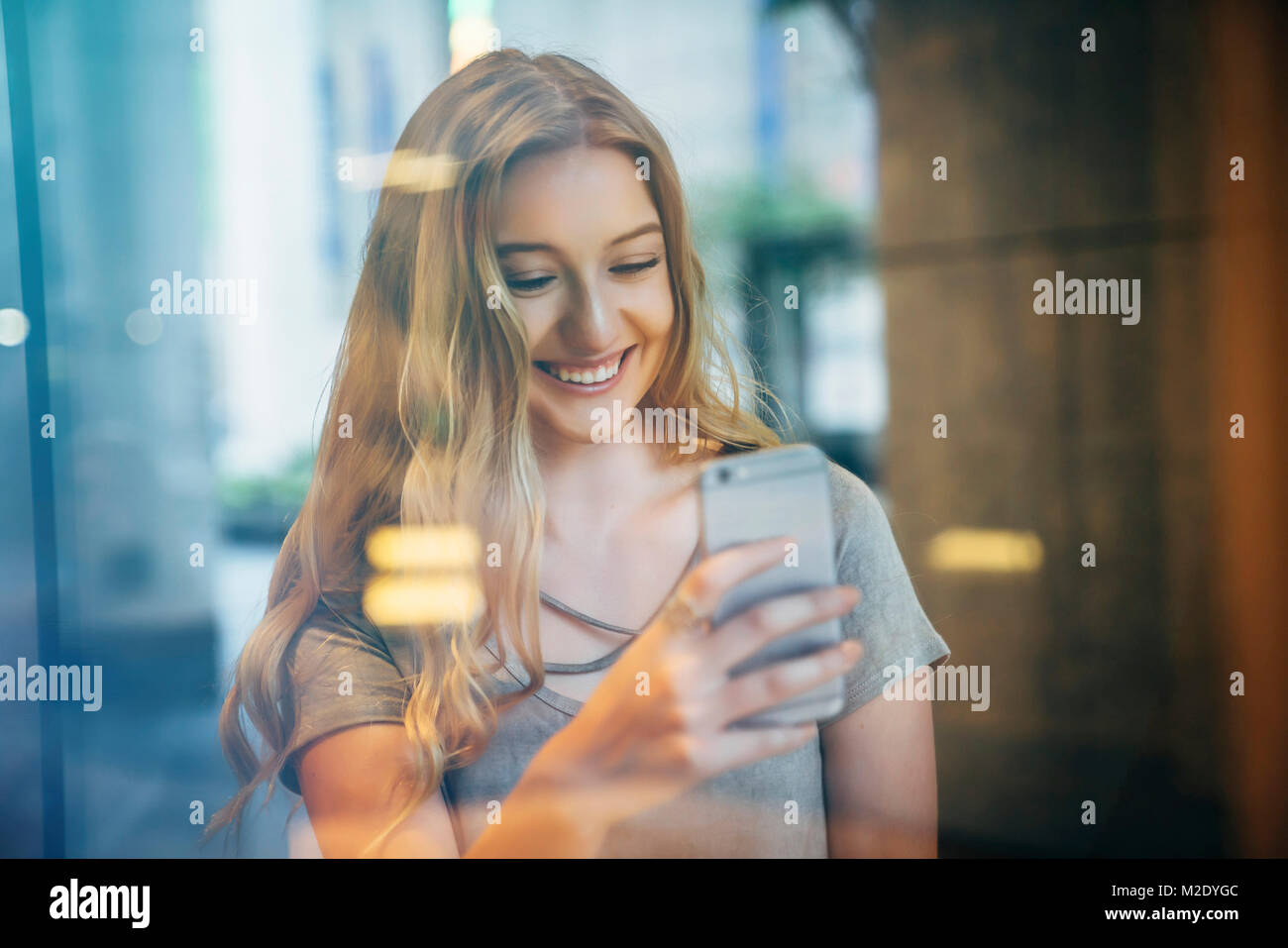 Smiling Caucasian woman posing for cell phone selfie behind window Stock Photo