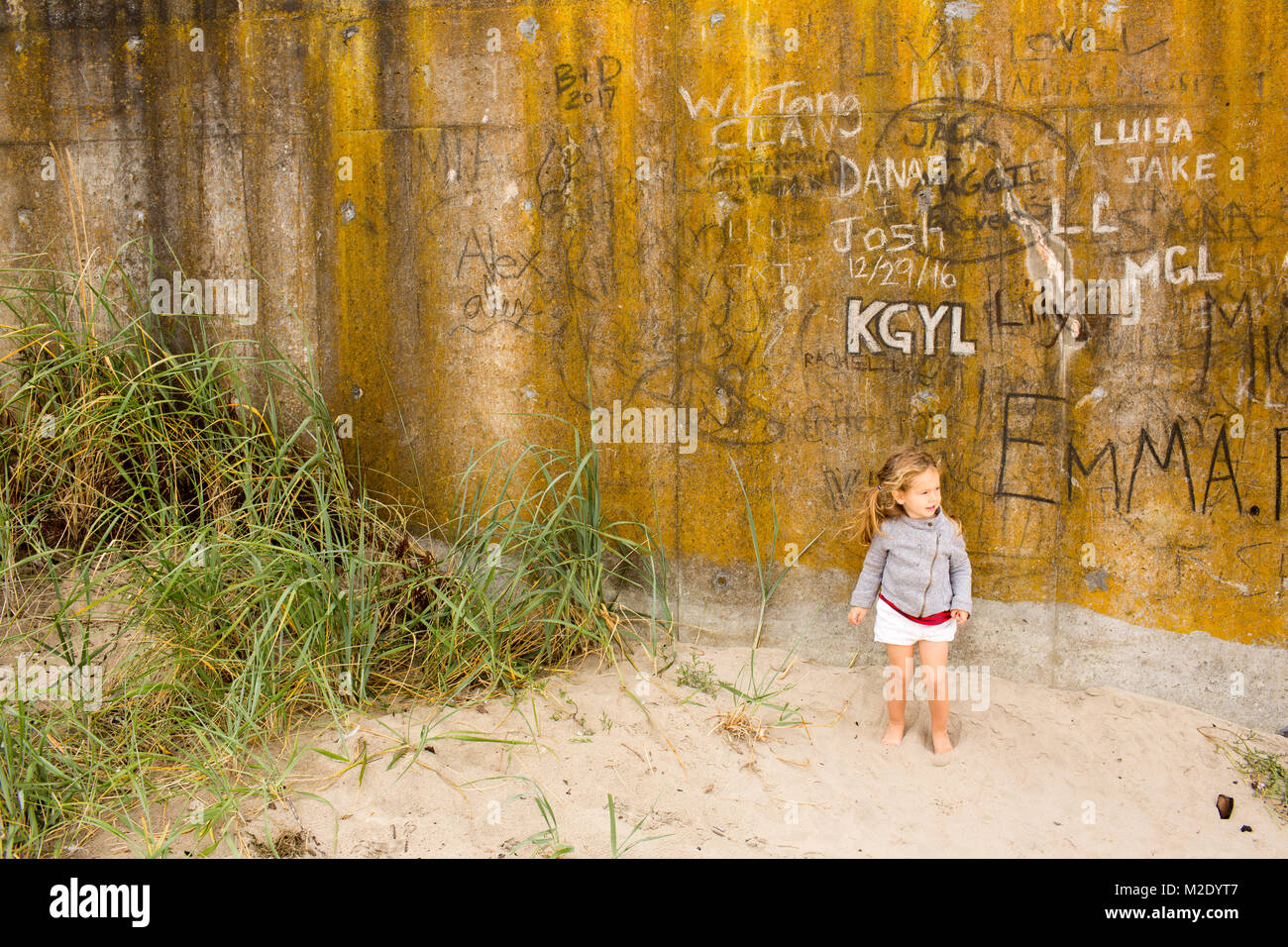 Caucasian girl standing in sand near graffiti wall Stock Photo