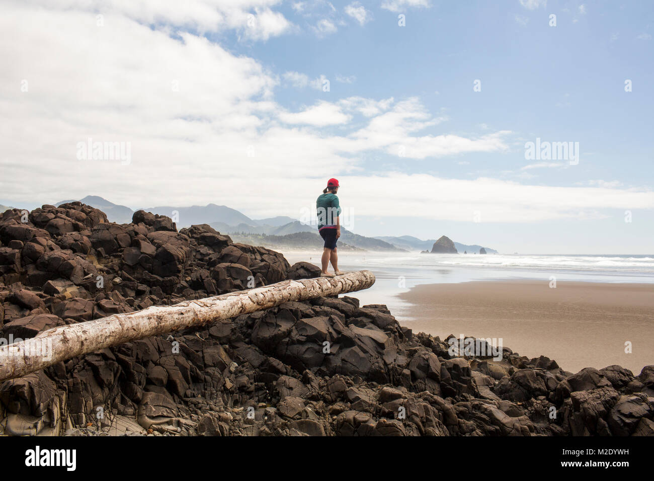 Caucasian woman balancing on log on rocks at beach Stock Photo