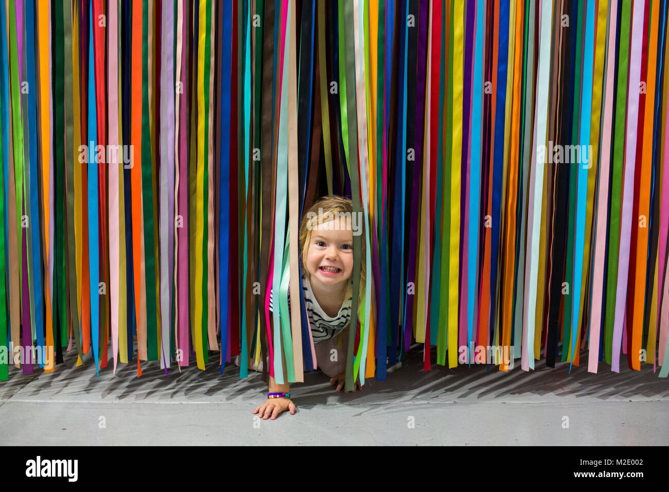Caucasian girl crawling under colorful hanging streamers Stock Photo