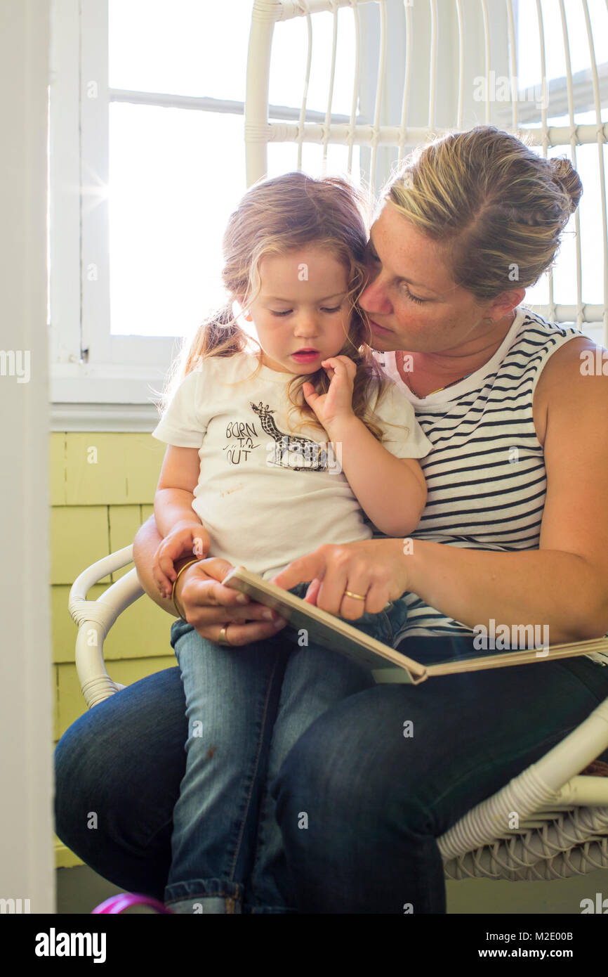 Caucasian mother reading book to daughter on lap Stock Photo
