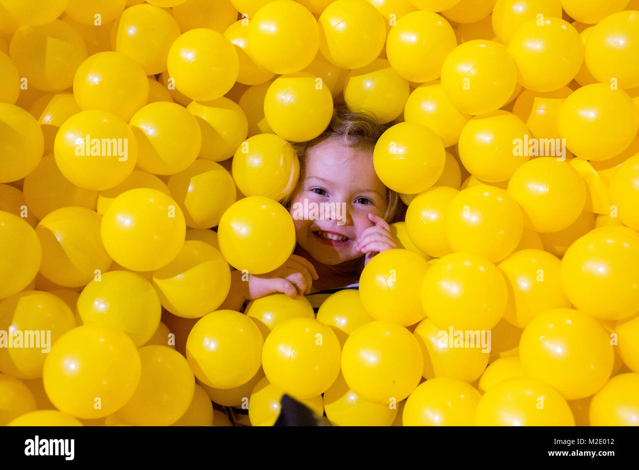 Caucasian girl laying in pile of yellow balls Stock Photo