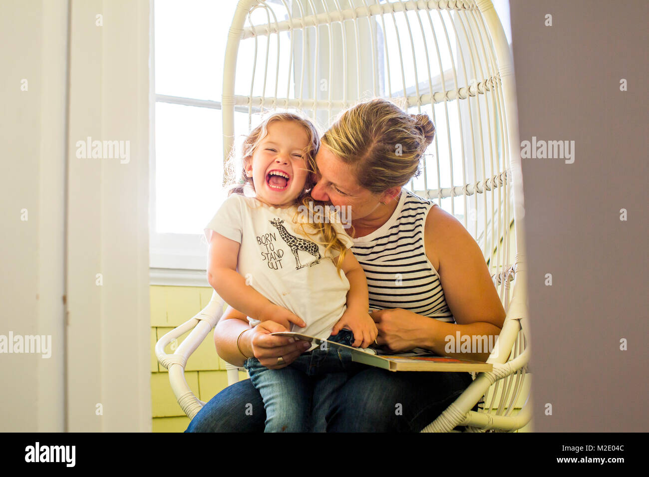 Playful Caucasian mother biting shoulder of daughter reading book Stock Photo