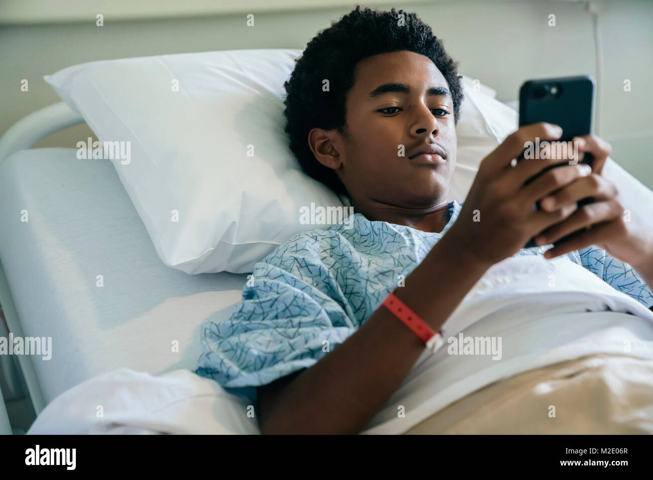 Black boy laying in hospital bed texting on cell phone Stock Photo