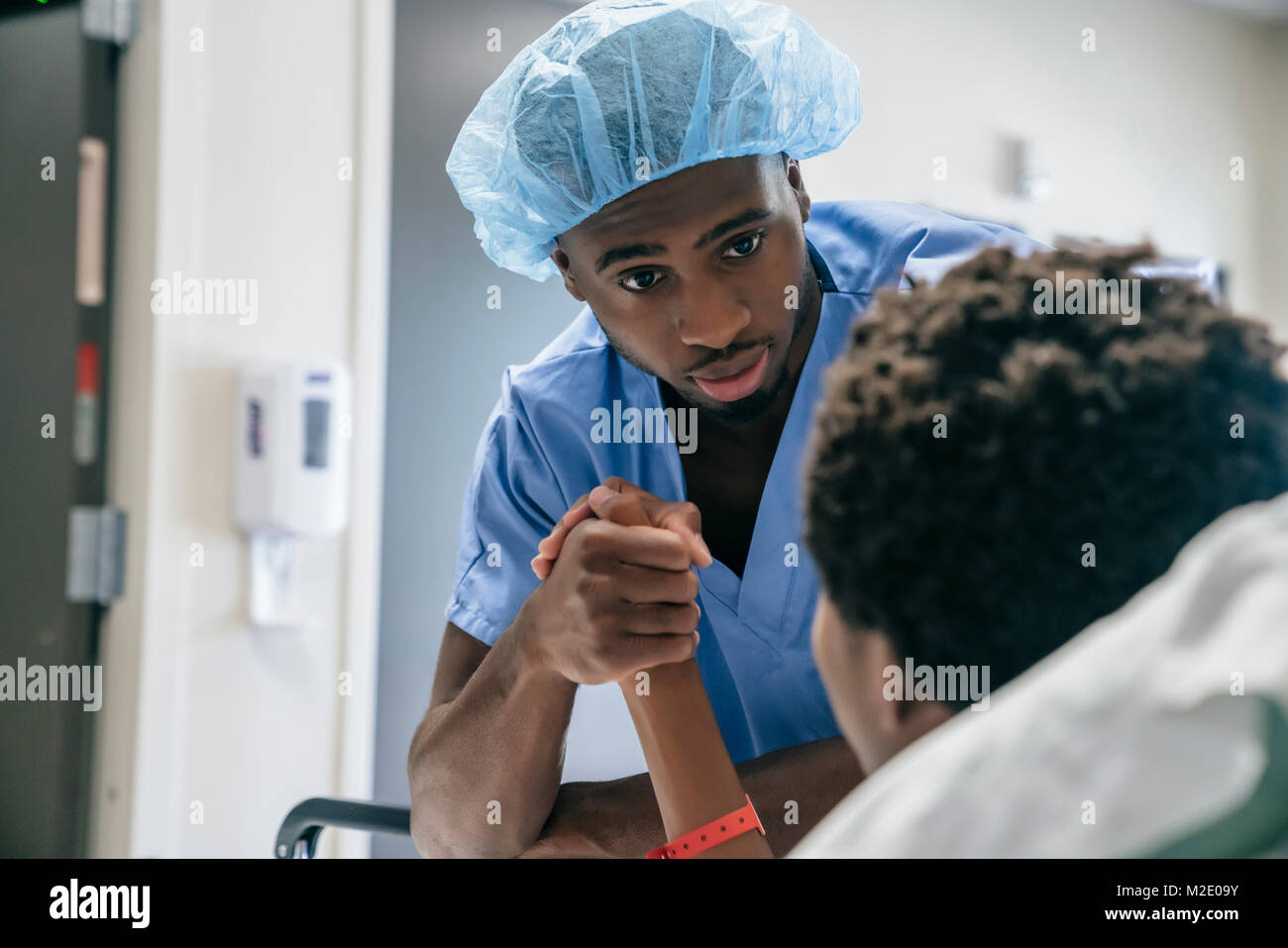 Black doctor holding hand of boy in hospital bed Stock Photo