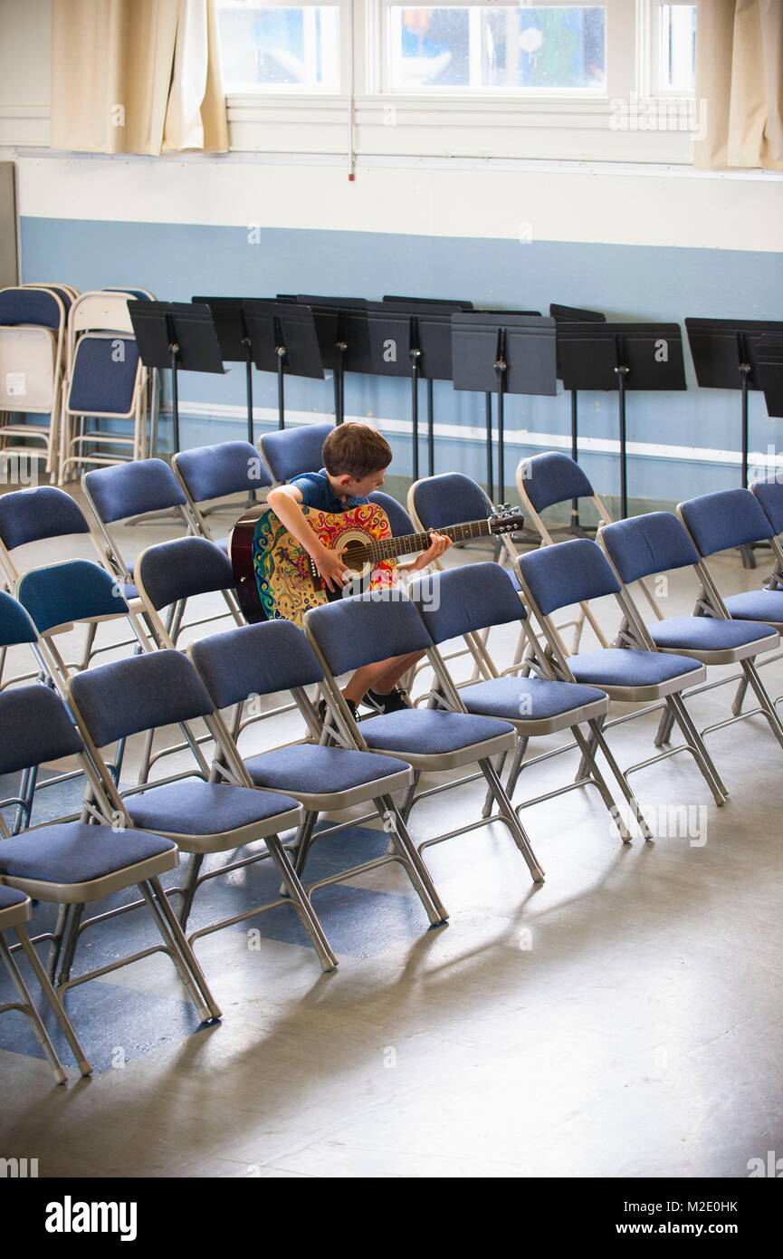 Caucasian boy sitting in row of chairs practicing guitar Stock Photo