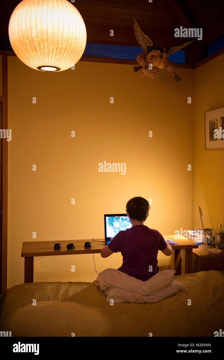 Caucasian boy sitting on bed using laptop Stock Photo - Alamy