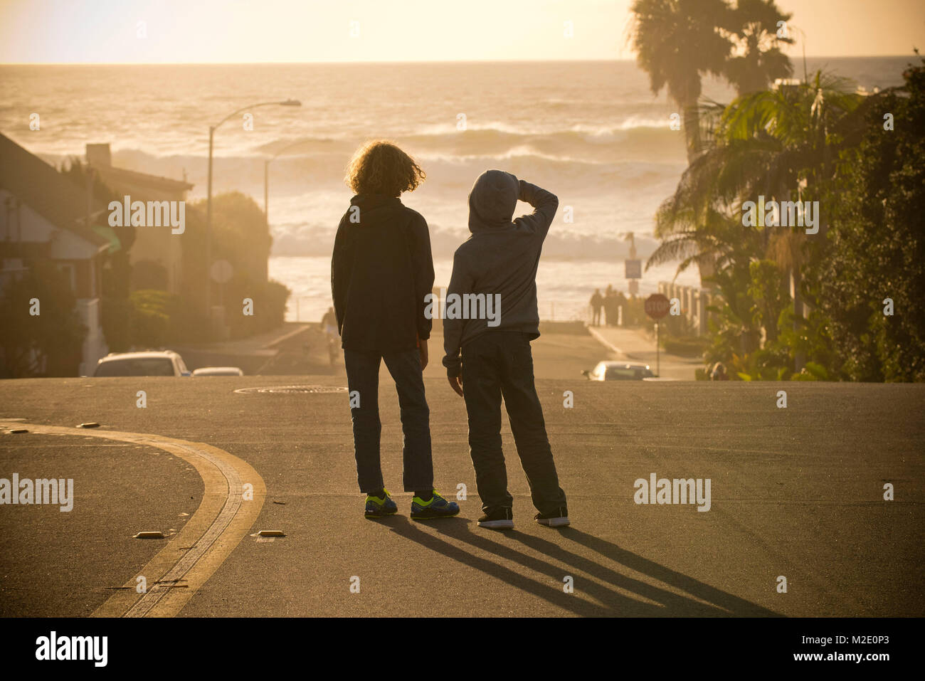 Boys standing in street admiring ocean waves Stock Photo