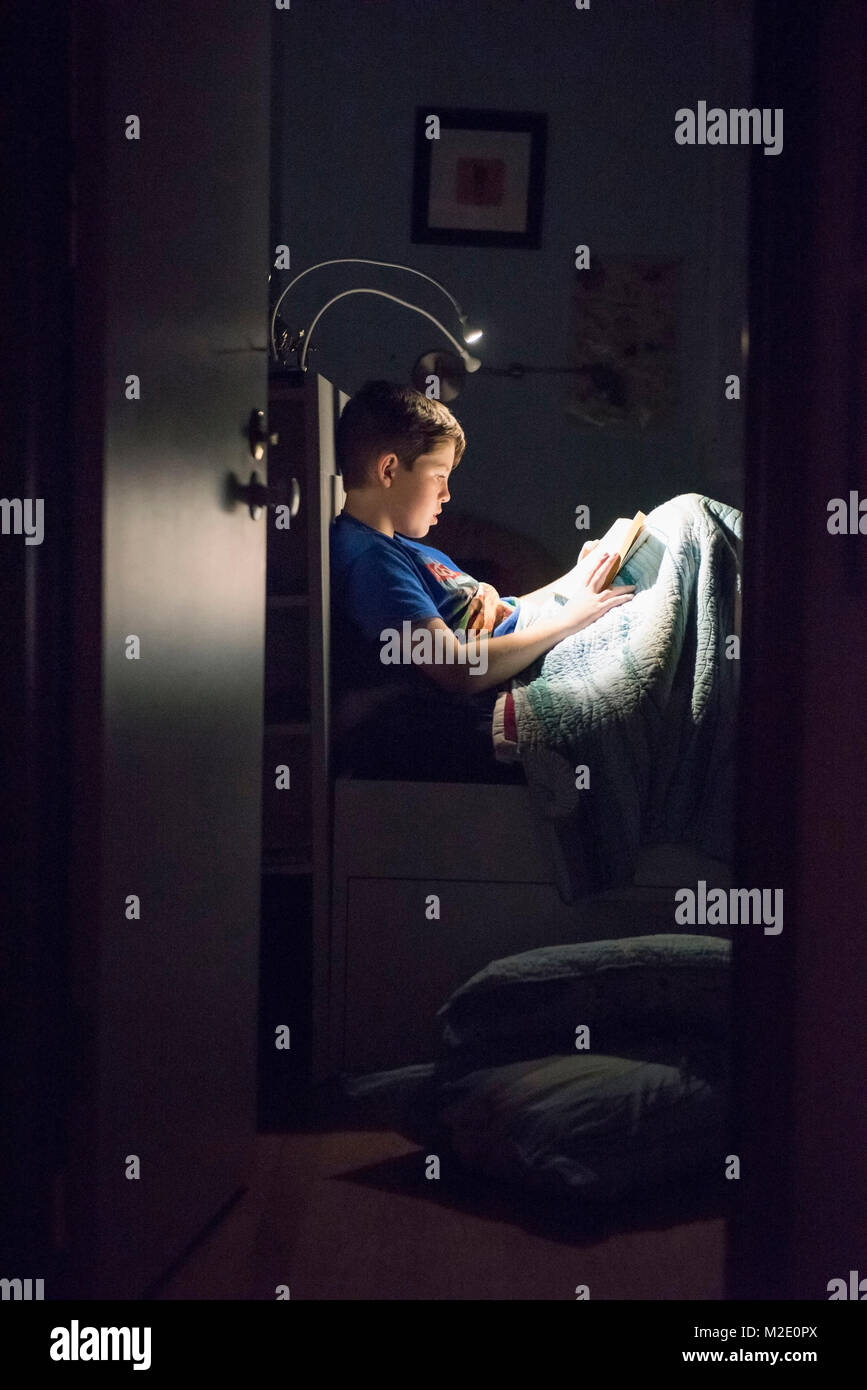 Caucasian boy reading book in bed at night Stock Photo