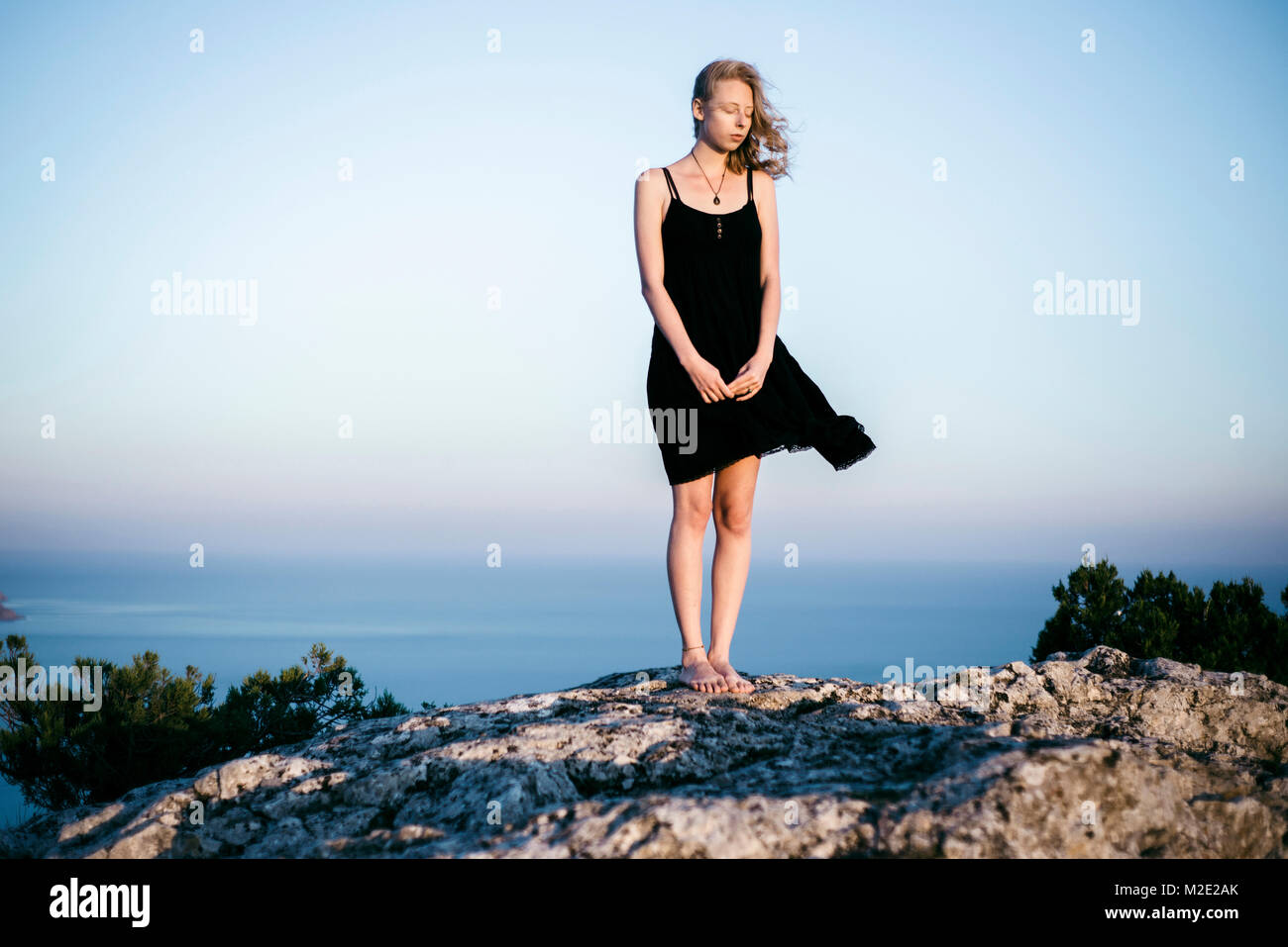 Wind blowing dress of Caucasian woman standing on rock near ocean Stock Photo