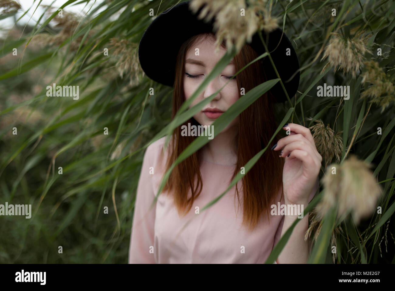 Pensive Asian woman standing in field of tall grass Stock Photo