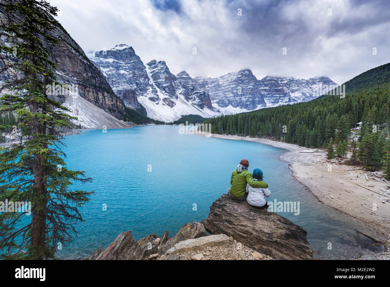 Asian couple sitting on rock admiring scenic view of mountain lake Stock Photo