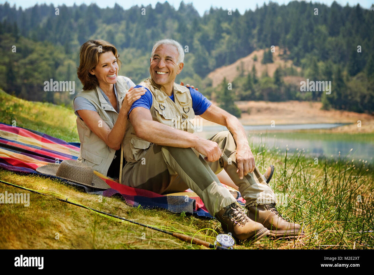 Couple sitting on blanket near lake with fishing rod Stock Photo